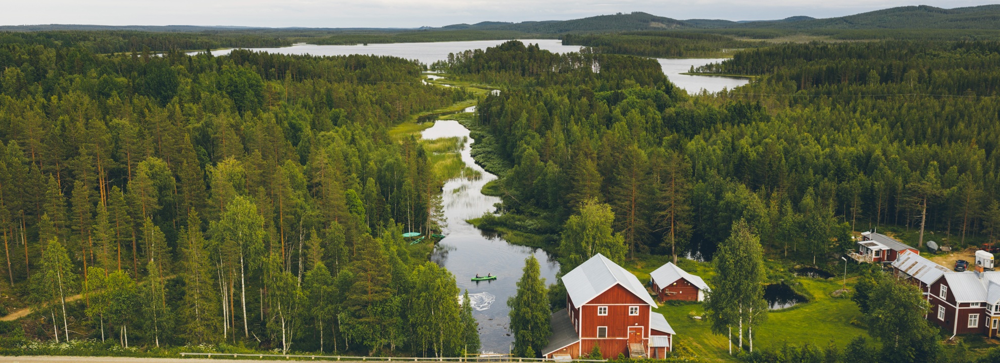 En flygbild av en sjö, ett slingrande vattendrag med en kanot och ett rött hus.