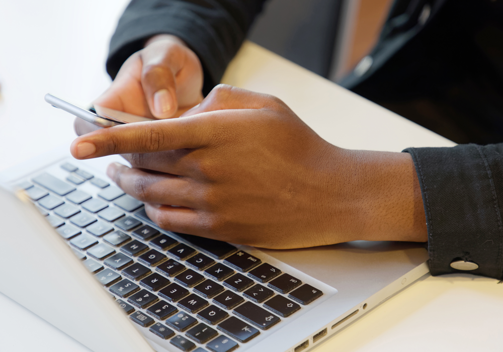 Närbild på elevs händer som skriver på mobiltelefon stöd på laptops tangentbord