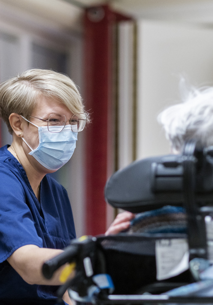 Fysioterapeuten Sofia bär munskydd när hon träffar patient. Patienten är rullstolsburen.