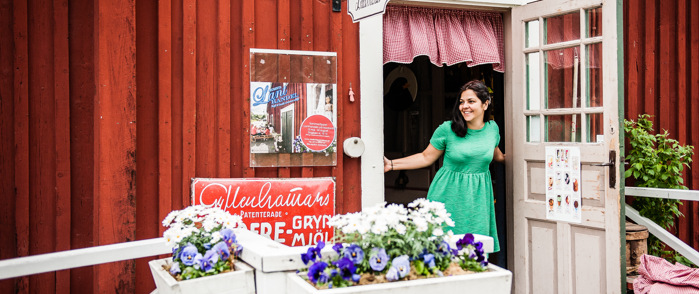En kvinna i grön klänning står i en dörröppning till Nordanås Lanthandel Café.