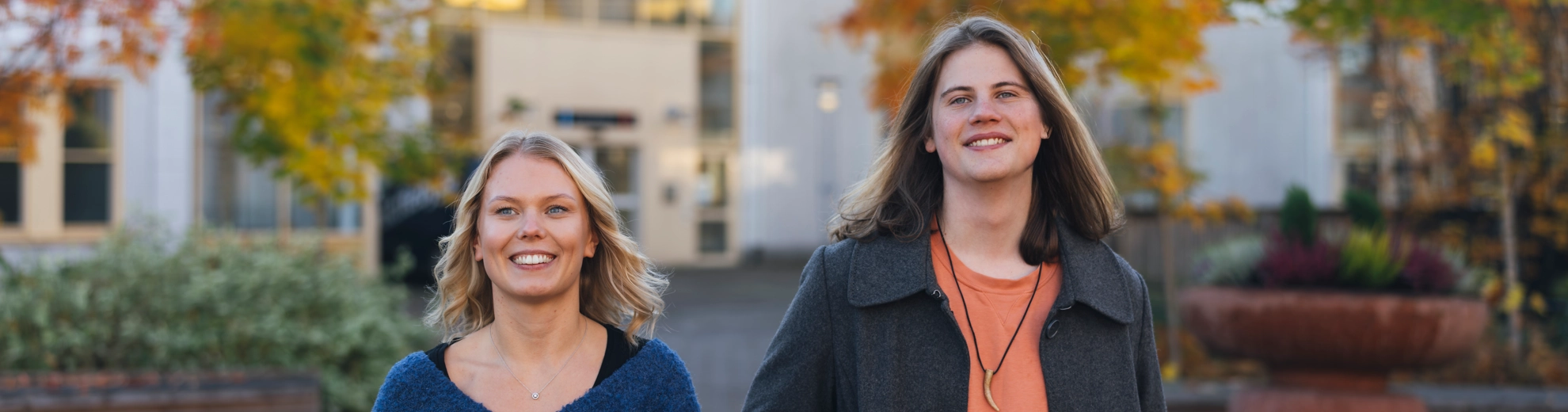 Två personer som går bredvid varandra genom campus utomhusmiljöer.