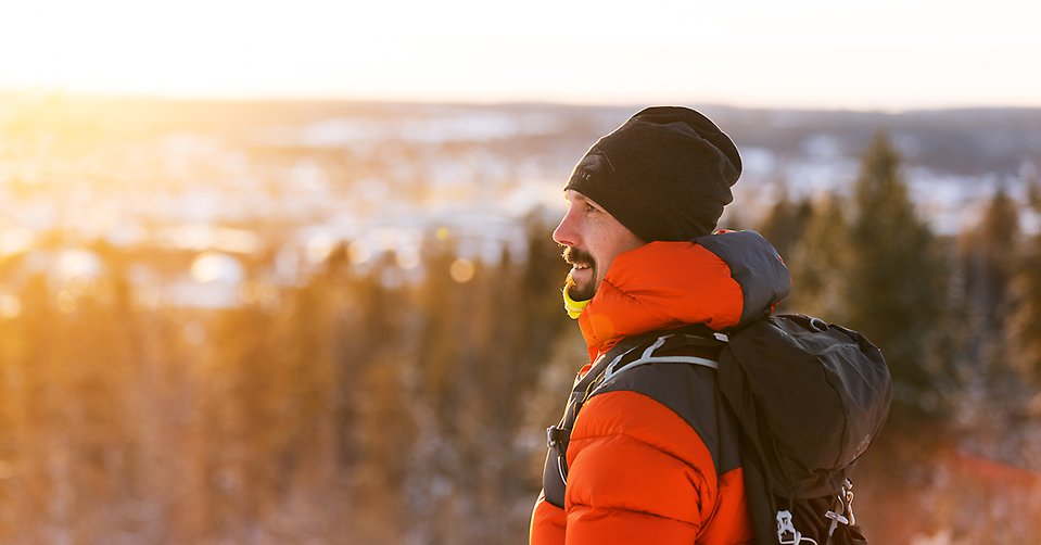 Marcus på skidtur, han tittar ut över snötäckt landskap med skog och berg med solen mot ansiktet