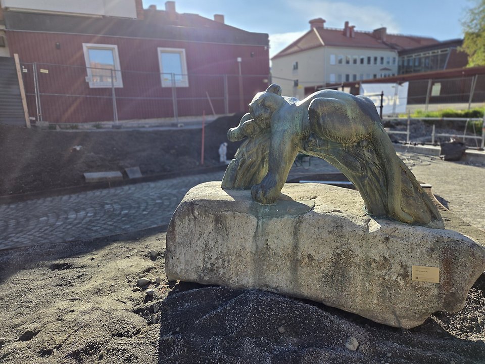En panterstaty står på en stor sten, med byggnader i bakgrunden.