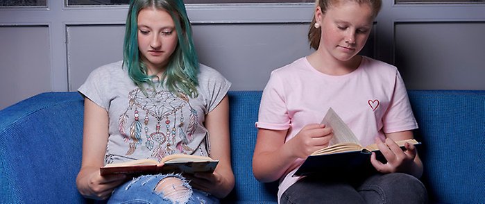 Två ungdomar sitter i en soffa och läser böcker.