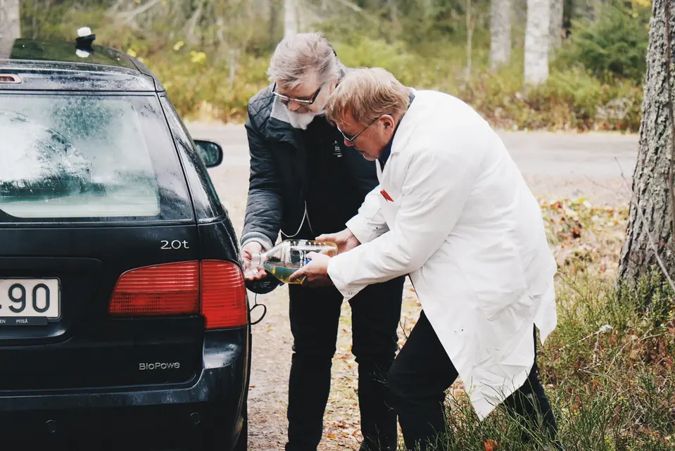 Två män som häller en vätska från en flaska i en biltank