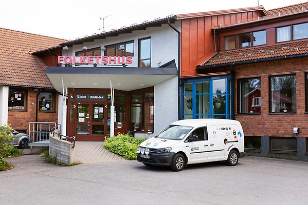 Fasaden på Ursvikens bibliotek. En bil står parkerad vid ingången.