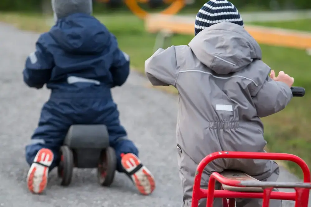 Barn som har varma overaller på sig och lär sig cykla på bobbycars